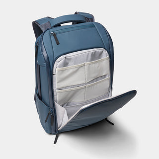 A slate blue backpack shown open to reveal a light gray interior organizer pocket with mesh and zip compartments, photographed on a clean light gray background.
