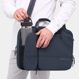 NOMATIC Laptop Bag in navy, carried by hand with water bottle in side pocket